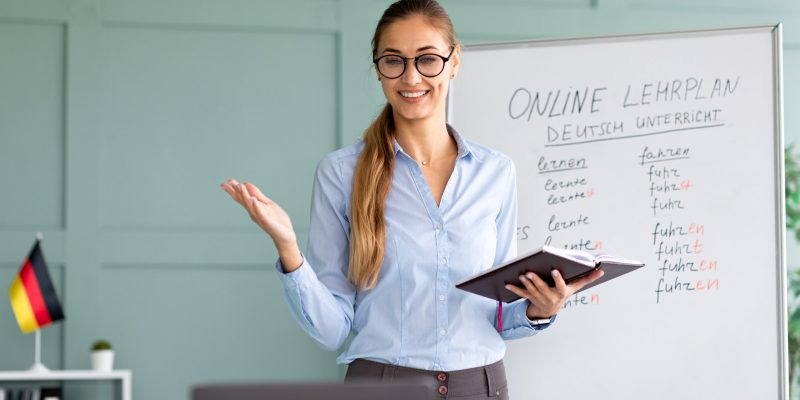 Studying German online. Cheerful female teacher giving online foreign language lesson, using laptop, explaining grammar to remote students on web